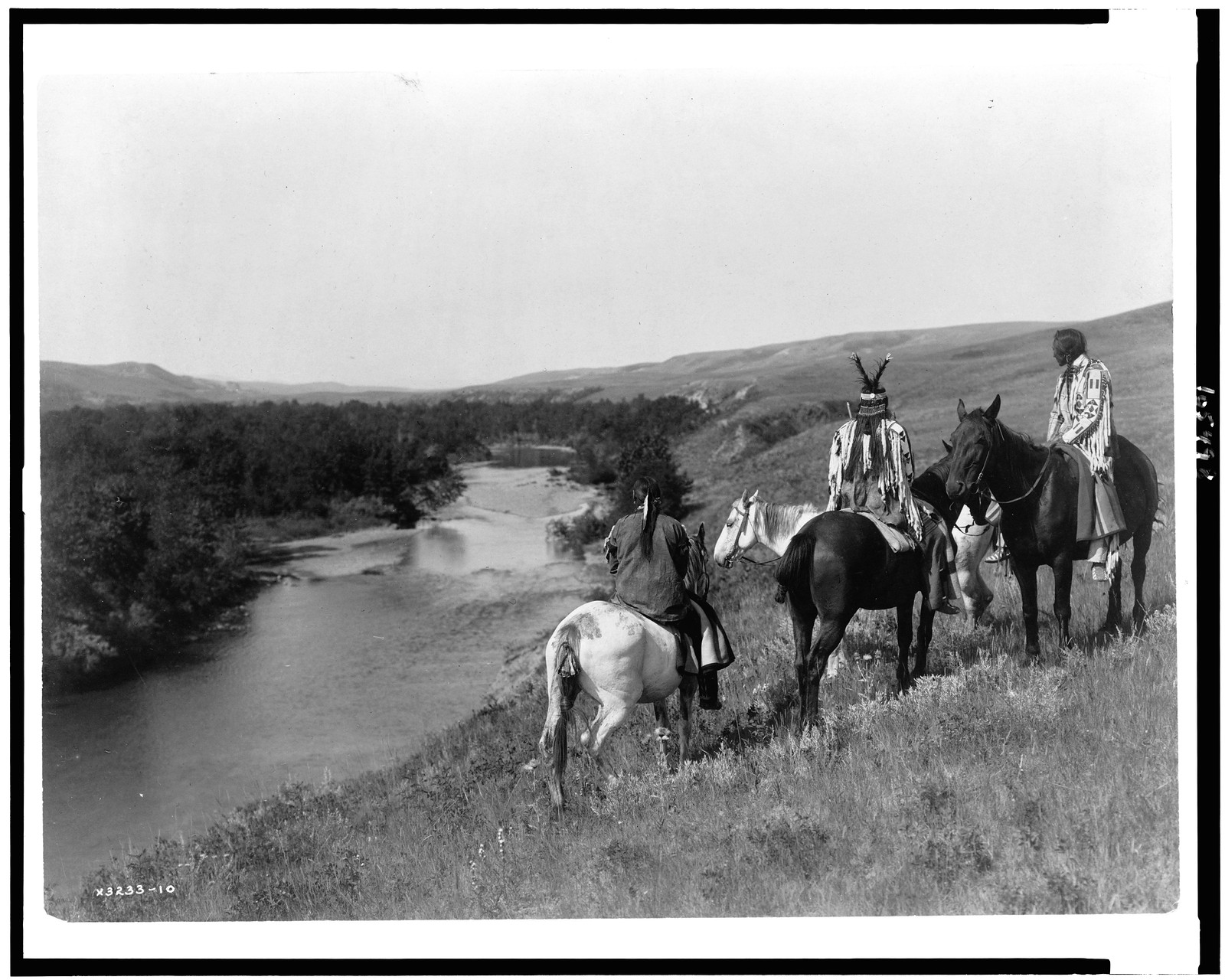 [Three Piegan Indians and four horses on hill above river], c1910. — historic photograph