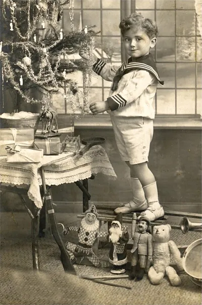 Boy in sailor suit decorating Christmas tree with toys