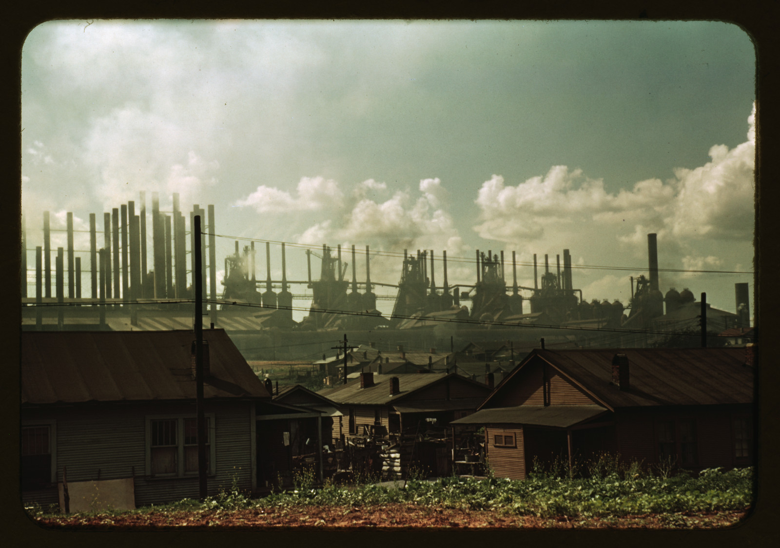 Steel mill stacks rising above small houses in foreground — historic image