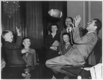 [Richard Milhaus Nixon, 1913-, seated, at desk in Capitol, playing football with Andrus Suritis, one millionth refugee relocated by an international welfare organization]