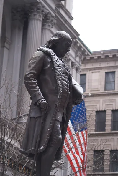 Bronze statue of Benjamin Franklin beside an American flag