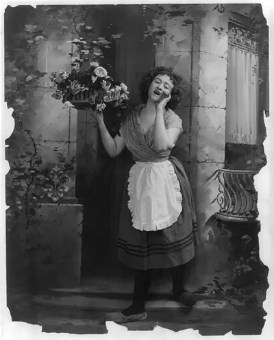 [Young woman modeling: Full lgth., standing, wearing Dutch costume and hawking tray of flowers]