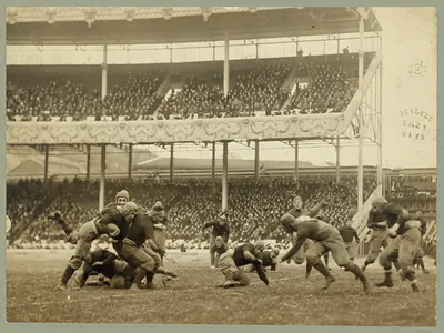 Football players tackling in a crowded stadium, sepia photograph