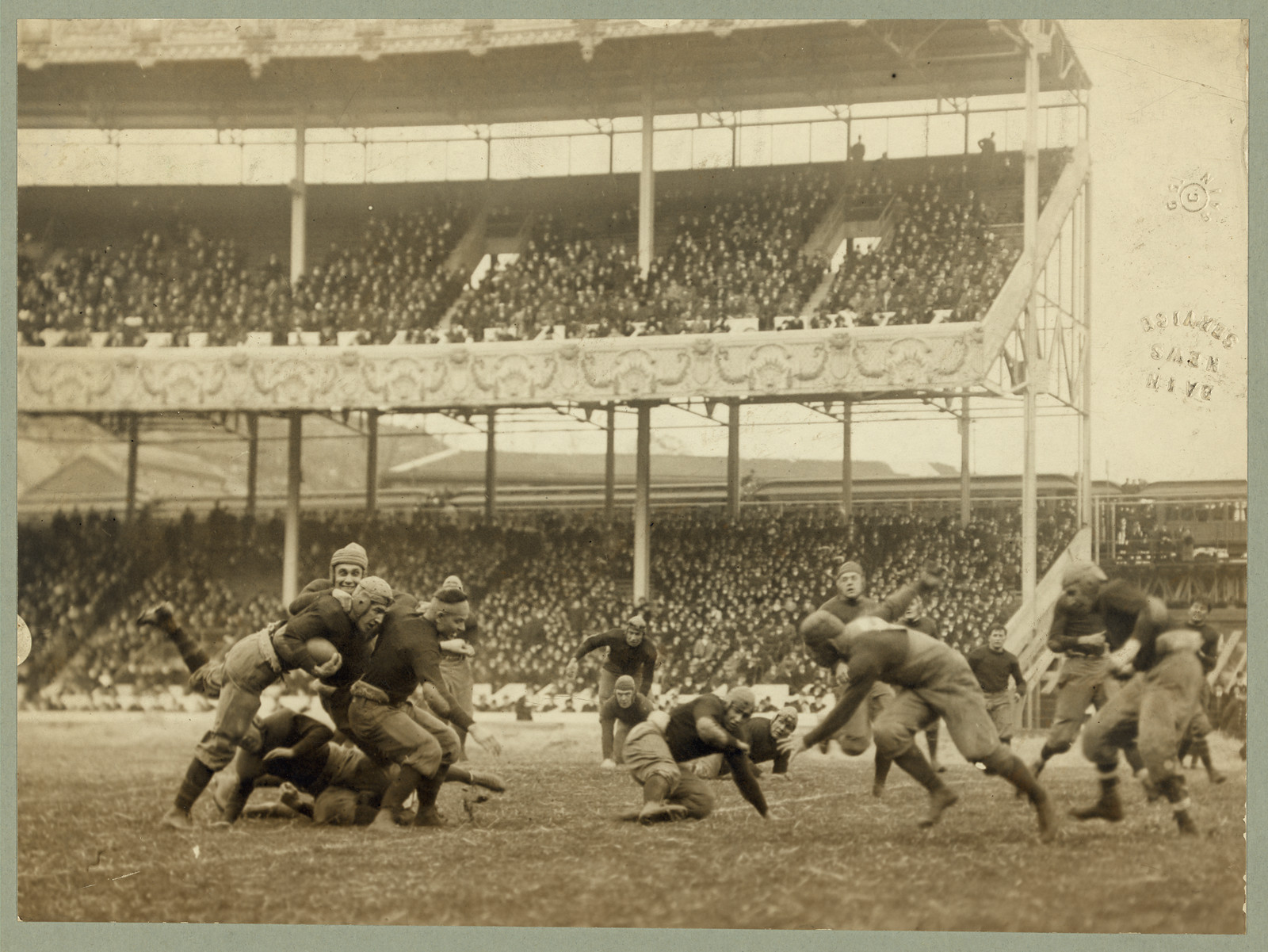 Football players tackling in a crowded stadium, sepia photograph, 1916 — historic photograph