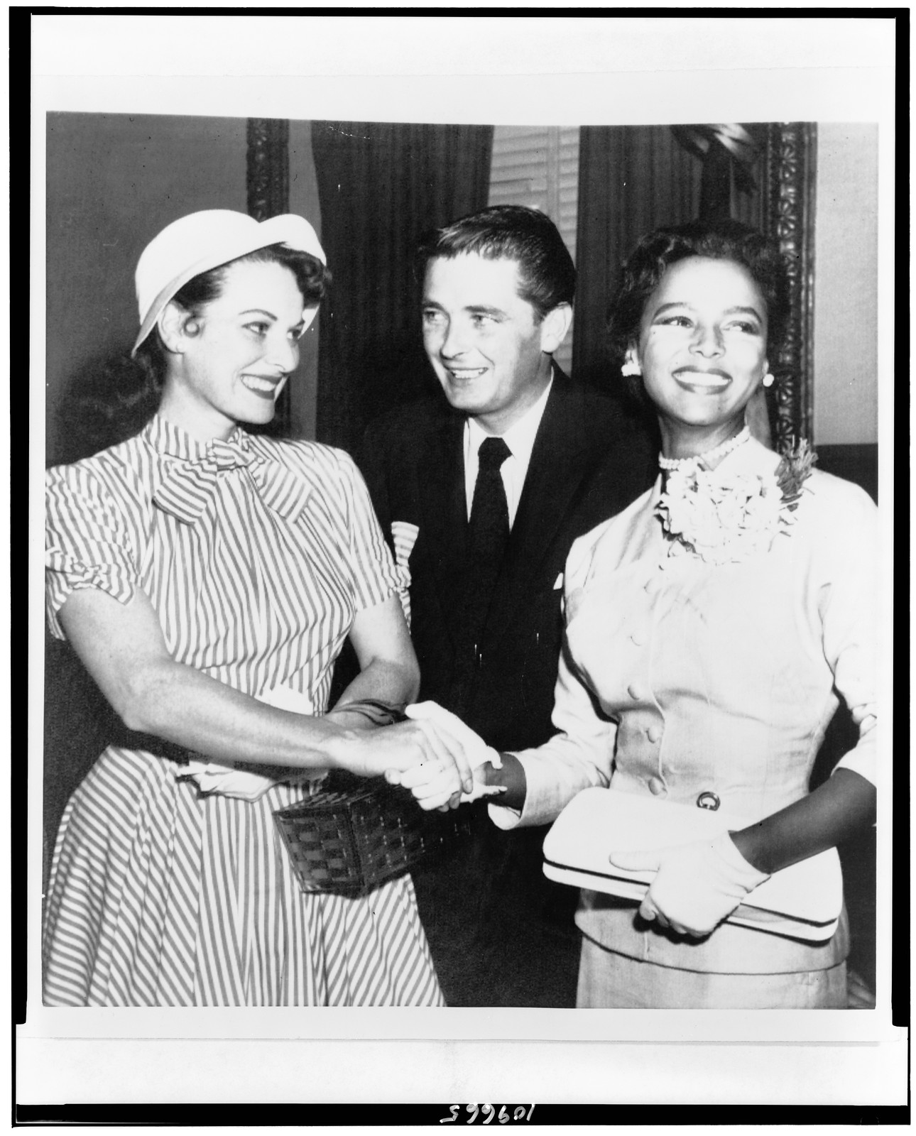 [Actresses Maureen O'Hara and Dorothy Dandridge join hands, outside courtroom, as if to seal a pact against Confidential Magazine, while Maureen's brother, James FitzSimons, looks on] — historic photograph