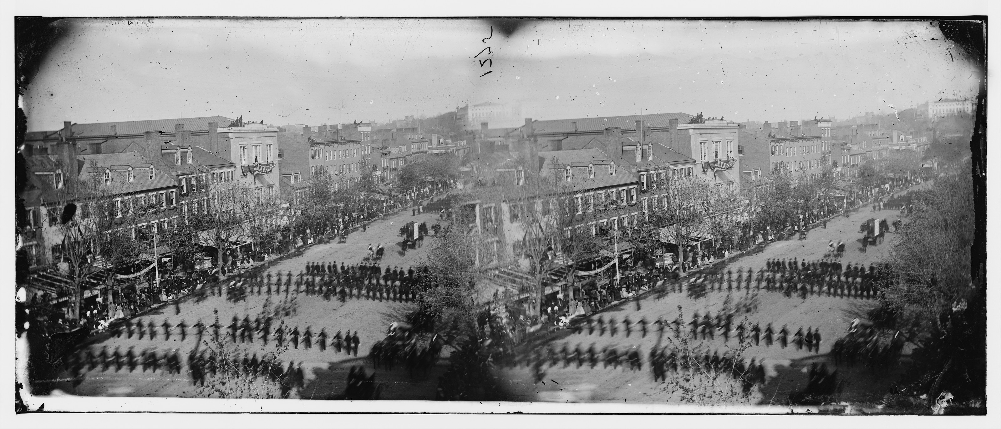 Military column marching down a city avenue, crowds on sidewalks — historic image