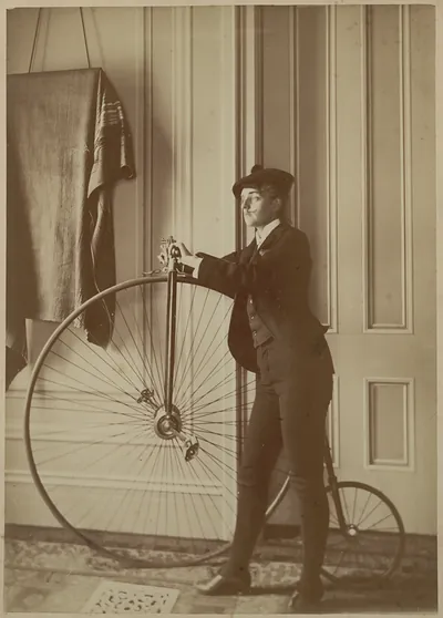 Man posing with a high-wheel bicycle indoors