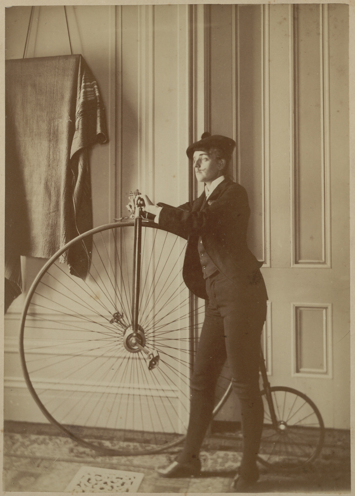 Man posing with a high-wheel bicycle indoors — historic image