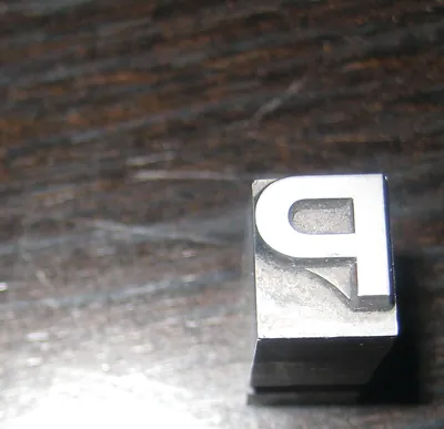Metal letterpress type block on dark wood surface