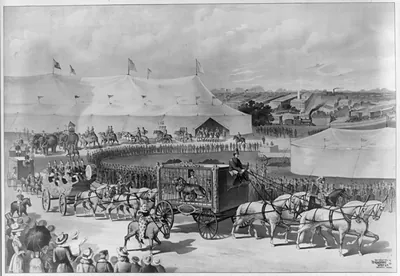 [Parade with lion in cage on wagon, circus tent in background]