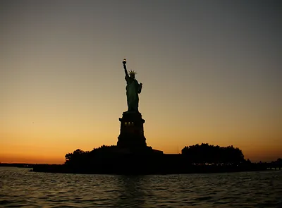 Statue of Liberty silhouetted against a sunset over water