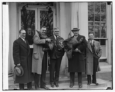 Four men holding turkeys on building steps, one in a hat