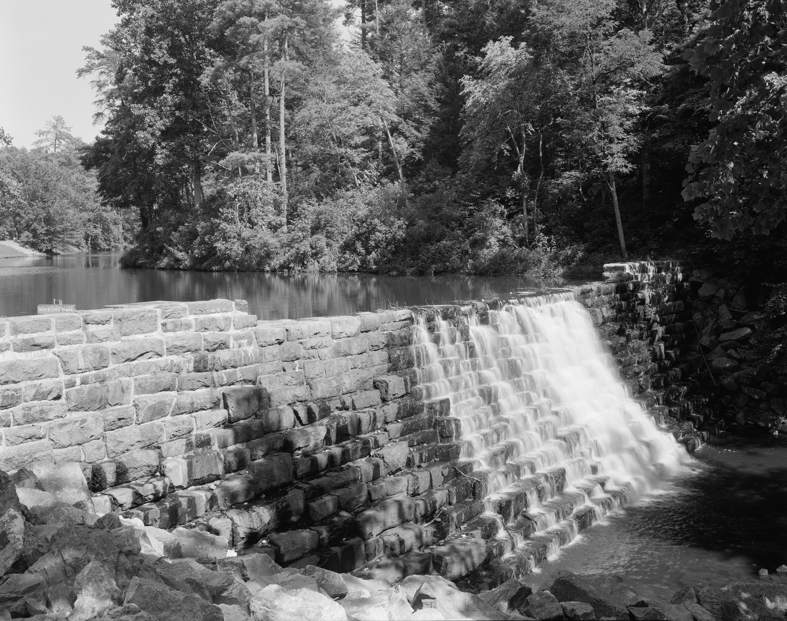 Stone dam with waterfall spillway in wooded setting — historic image