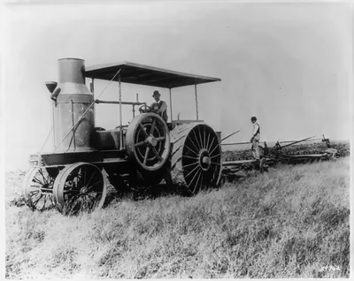 Early gas tractor. Man in derby at wheel, big stack in front