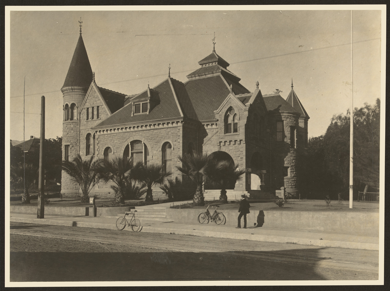 Stone building with turrets, palms and bicycles in street — historic image