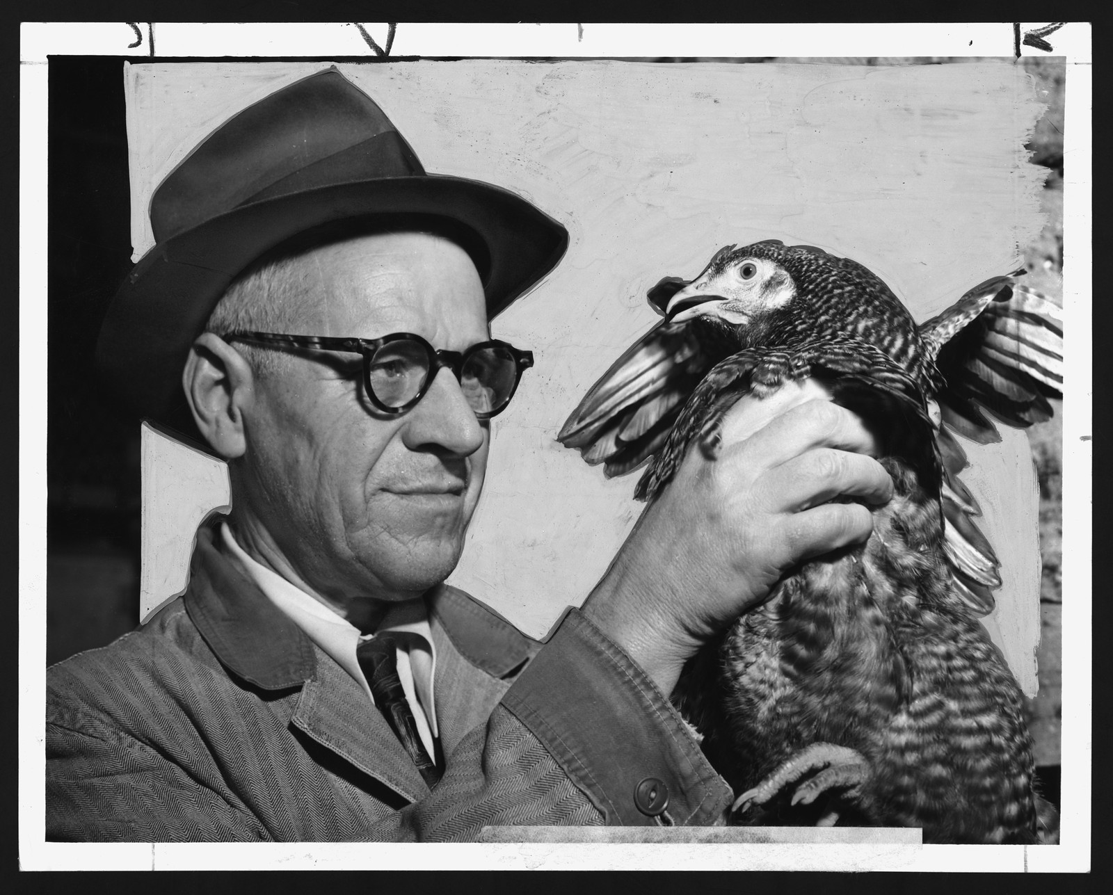 Man in hat and glasses holding a live poultry bird — historic image