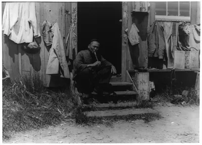 Man smoking pipe in shack doorway, San Pedro Chinatown