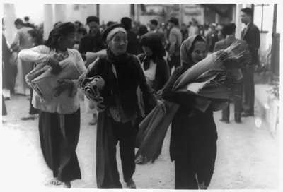 [Vietnam: Three women carrying goods in foregrd. on street; others in backgrd.]