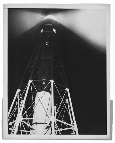 Lighthouse tower with lit beam at night, black and white photograph