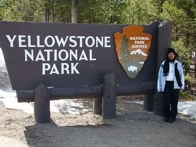Yellowstone National Park entrance sign with a person standing beside it