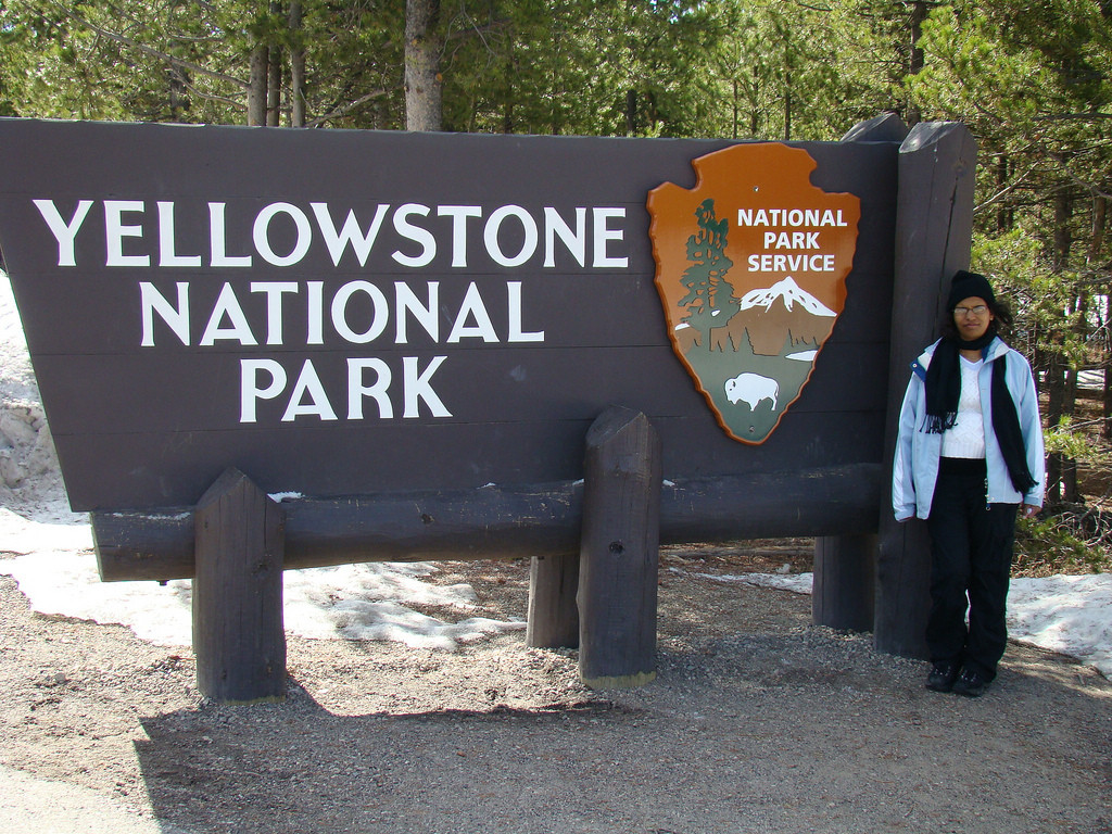 Yellowstone National Park entrance sign with a person standing beside it — historic image