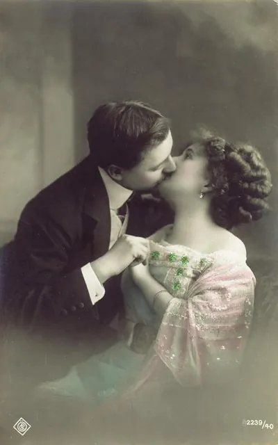Hand-tinted postcard of a couple kissing, with green clovers
