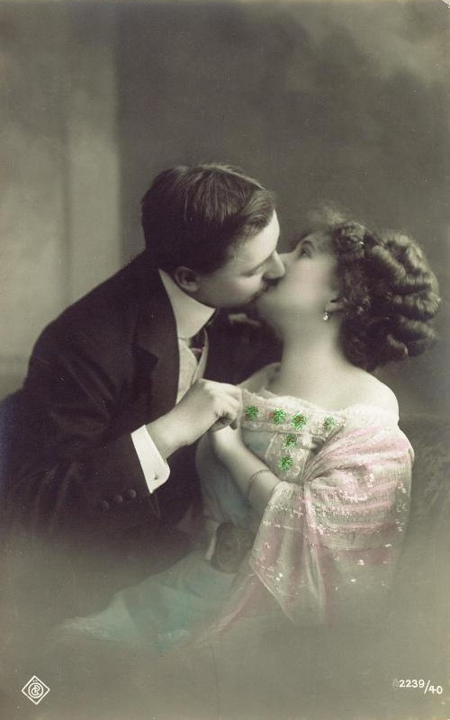 Hand-tinted postcard of a couple kissing, with green clovers — vintage postcard