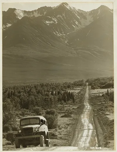 Army truck on gravel road below snowy mountains