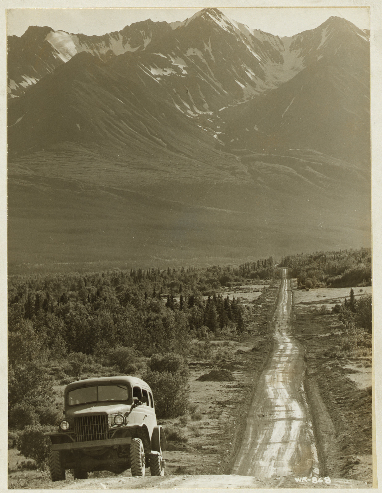 Army truck on gravel road below snowy mountains — historic image