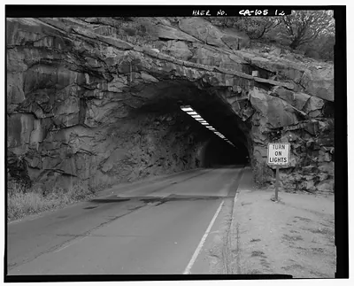 Rock tunnel on road with 'Turn On Lights' sign