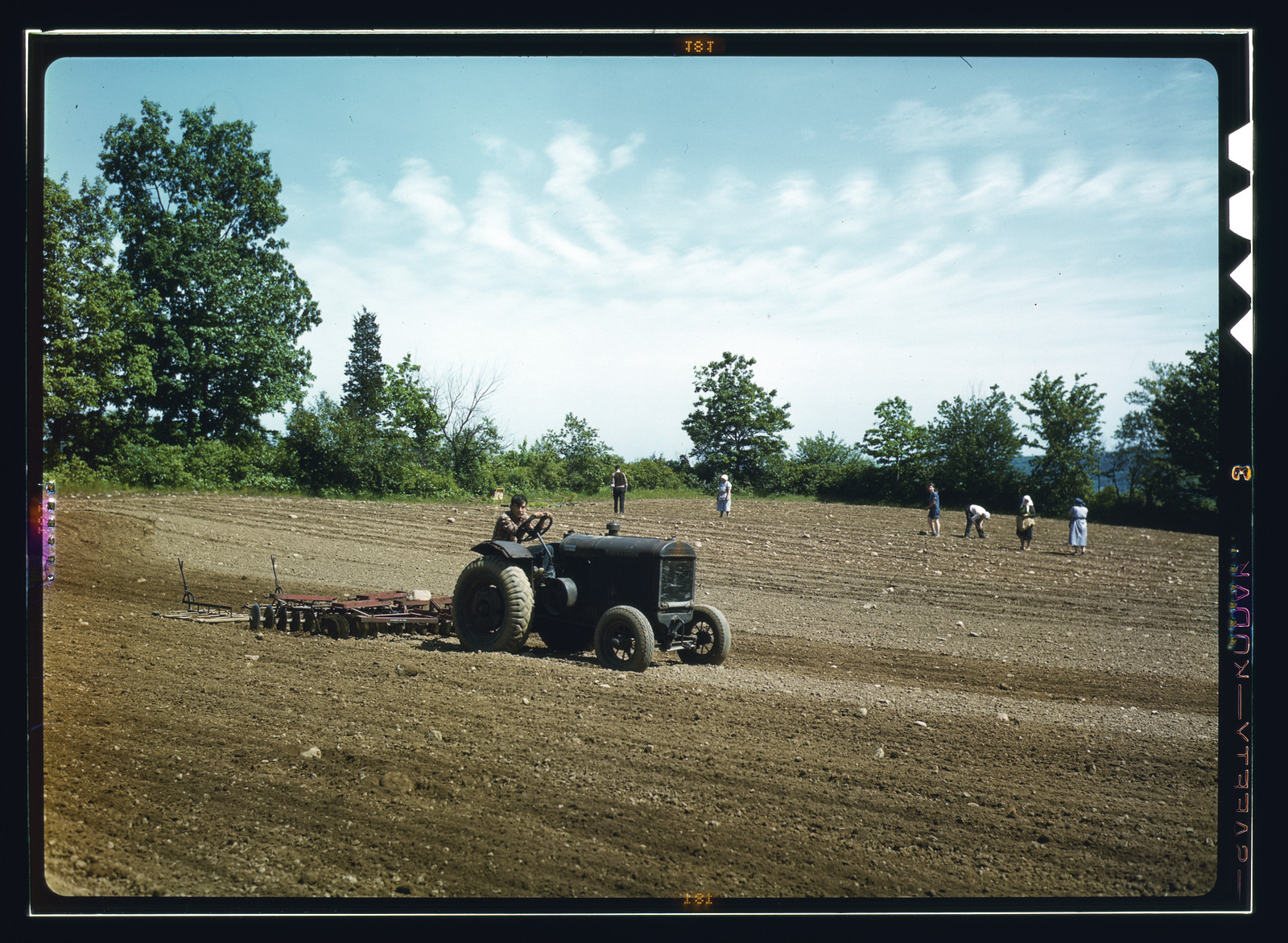Tractor pulling a harrow across a farm field — historic image