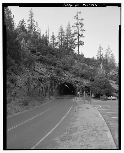 Rock tunnel through hillside on mountain road, with parking area