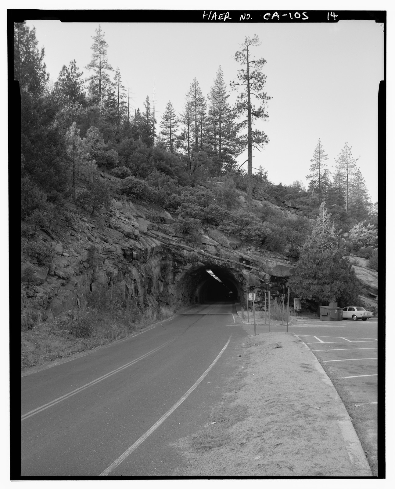 Rock tunnel through hillside on mountain road, with parking area — historic image