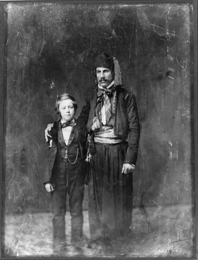 [Unidentified man in Middle Eastern costume with arm around boy, full-length portrait]