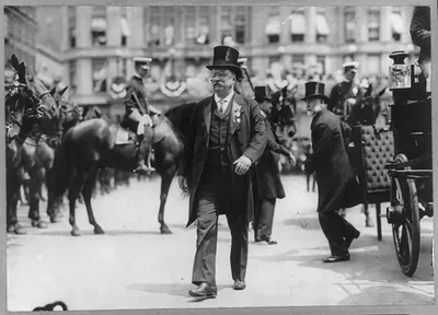[Theodore Roosevelt, full, walking in front of men on horseback on street, facing left]