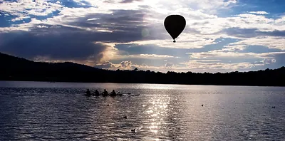 Rowers on a lake with a hot air balloon at sunset