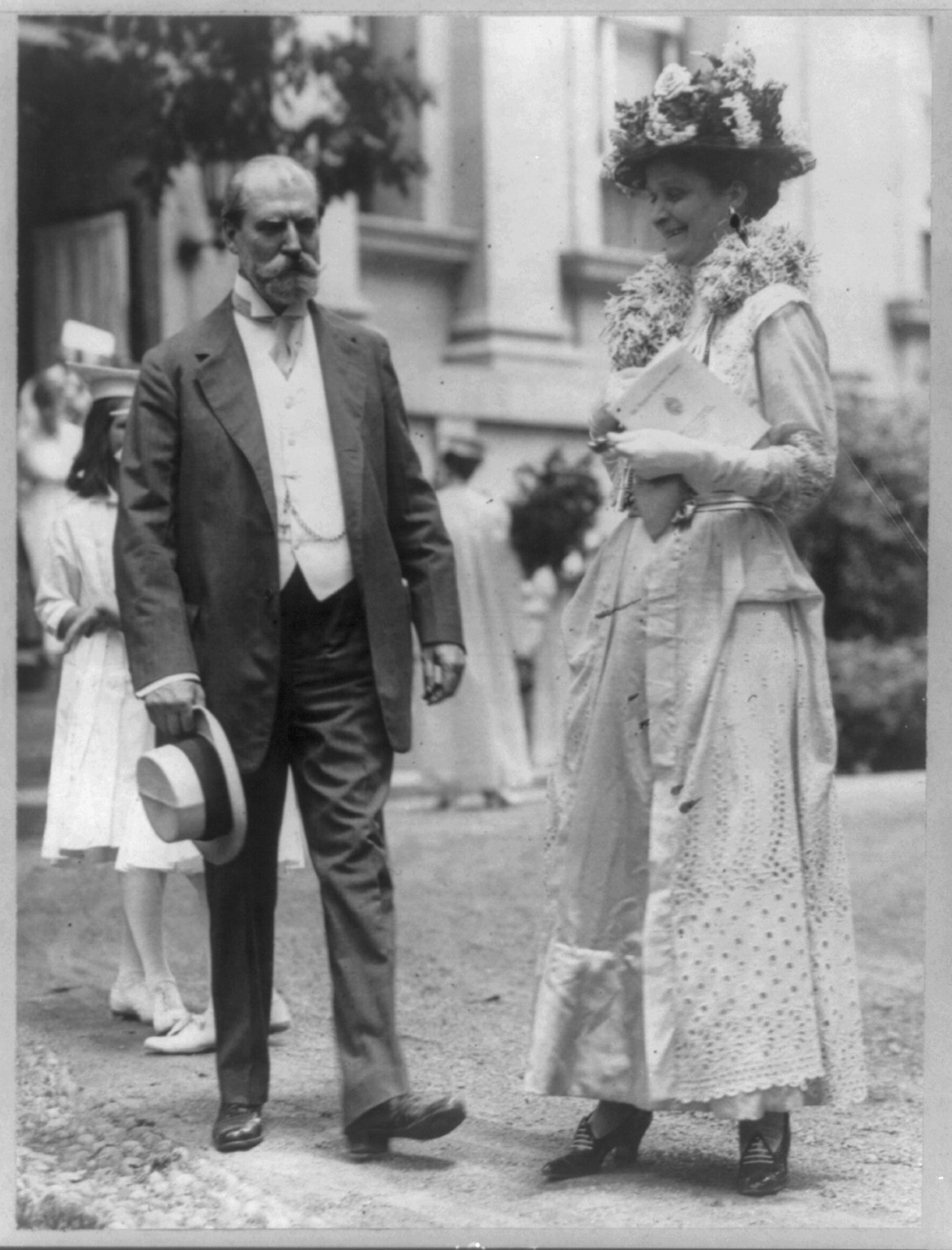 [Charles Evans Hughes, 1862-1948, full-length portrait, standing, facing right, and wife Antoinette (Carter) Hughes], c1916. — historic photograph