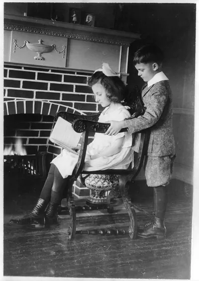 Evora and Porfirio Bonet [looking at book in front of fireplace]