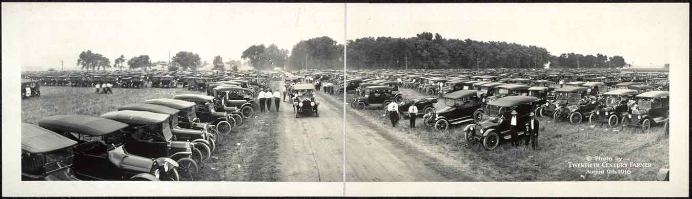 Panoramic photograph of rows of parked automobiles in a field — historic photograph