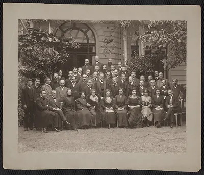 Large group photograph of men and women seated and standing outdoors before a building