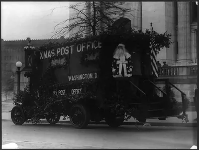 [Santa Claus standing on back of Washington, D.C., Post Office truck, decorated with branches and American flag]