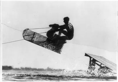 Man aquaplaning on a wooden board, jumping a ramp