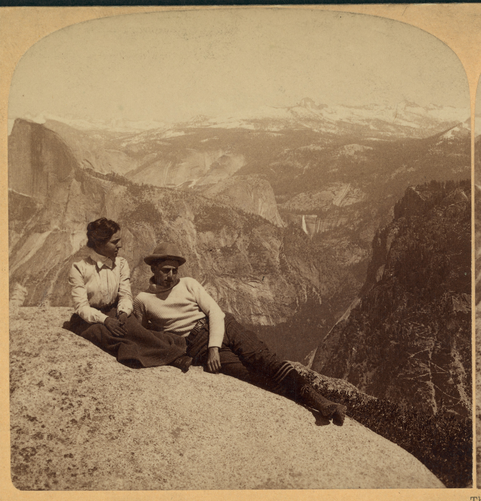 Couple seated on granite overlooking Yosemite Valley and Half Dome — historic image