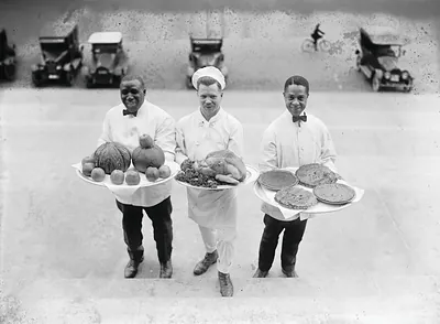 Three waiters carrying trays of food on steps