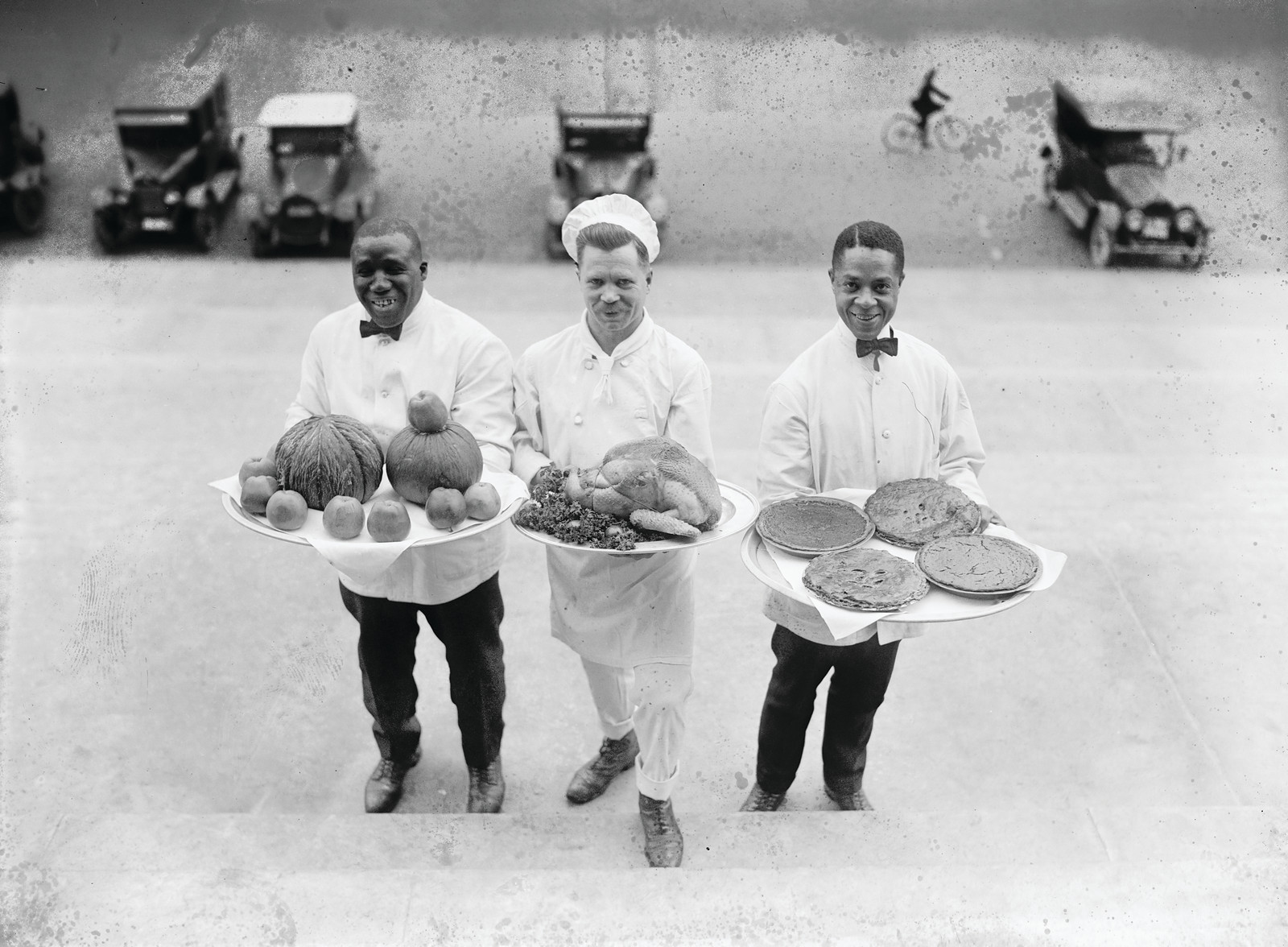Three waiters carrying trays of food on steps — historic image