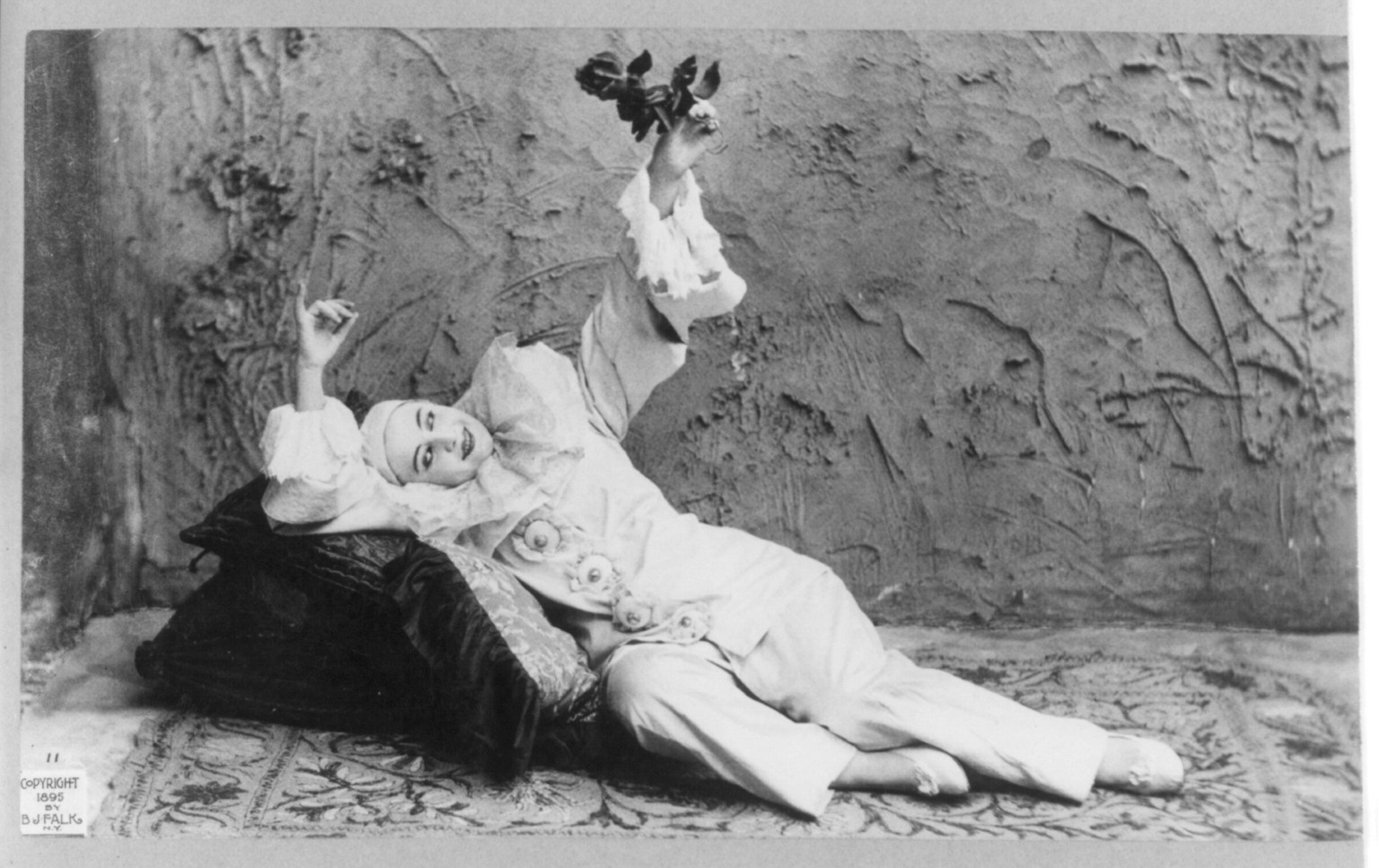 Pilar Morin as clown/mime: full length, lying, facing front; holding flower, c1895. — historic photograph