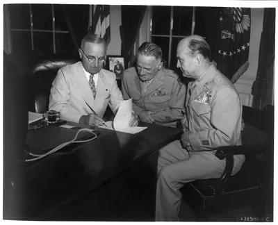 [Pres. Truman seated with 2 generals at desk, signing paper]