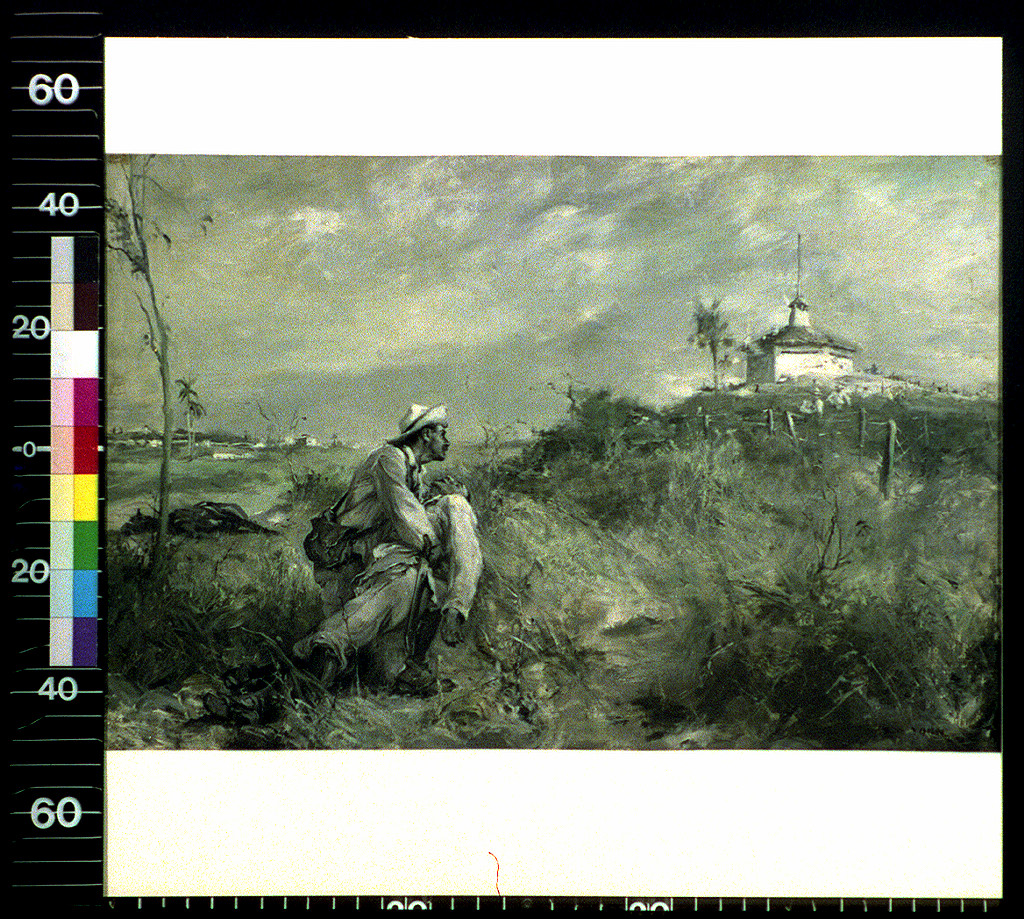 Man in white hat kneeling in grass before a white blockhouse — historic image