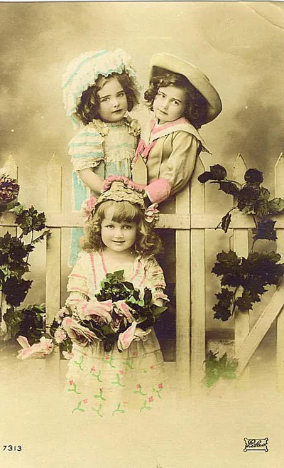 Three young girls posing by a white picket fence