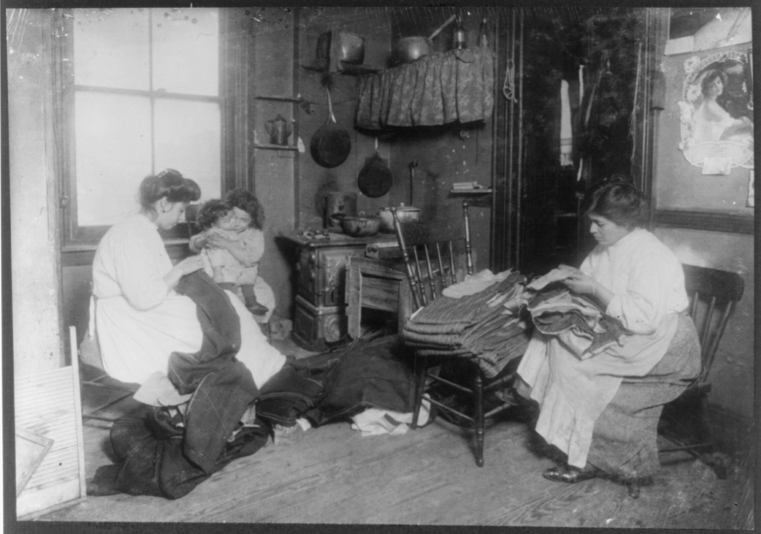 Mrs. Giuseppi (?) and Mrs. Di Angi (?), room 25, 2-4 Prince St., N.Y., finishing pants in dirty kitchen. Work lying around on the floor. Anaemic baby being cared for by neighbor child. Location: New York, New York (State), 1912 March. — historic photograph